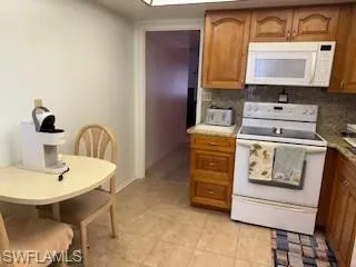 Kitchen featuring white appliances, backsplash, and brown cabinetry