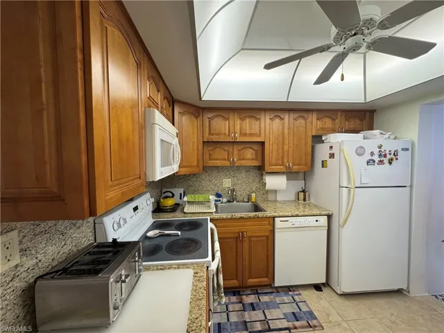 Kitchen featuring backsplash, brown cabinetry, white appliances, ceiling fan, and light tile patterned flooring