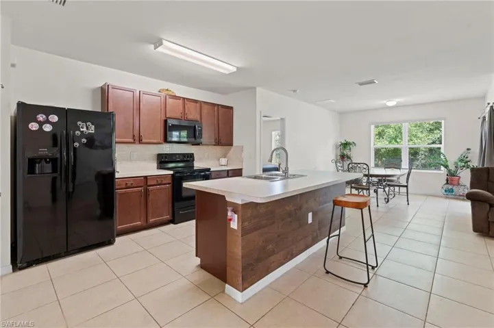 Kitchen with black appliances, backsplash, light tile patterned floors, a breakfast bar area, and light countertops