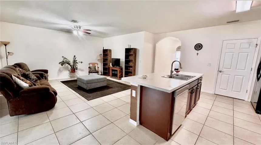 Kitchen with open floor plan, an island with sink, light countertops, arched walkways, and light tile patterned floors