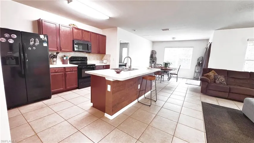 Kitchen with black appliances, open floor plan, a breakfast bar area, light countertops, and an island with sink