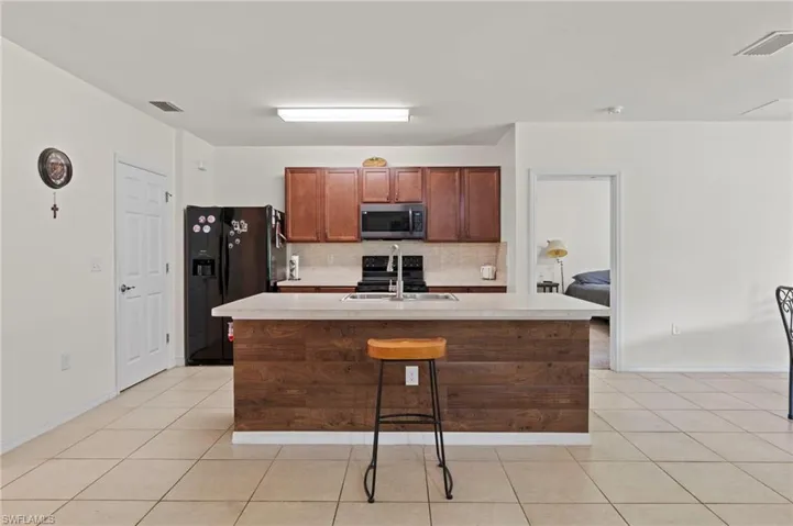 Kitchen with backsplash, black appliances, light countertops, a kitchen island with sink, and light tile patterned floors