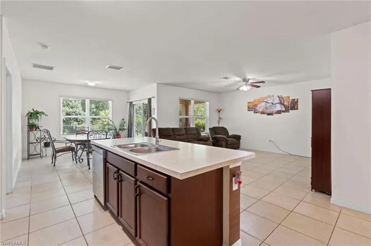 Kitchen featuring light countertops, dark brown cabinetry, open floor plan, a center island with sink, and light tile patterned floors
