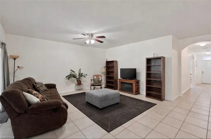 Living room with arched walkways, light tile patterned flooring, and a ceiling fan