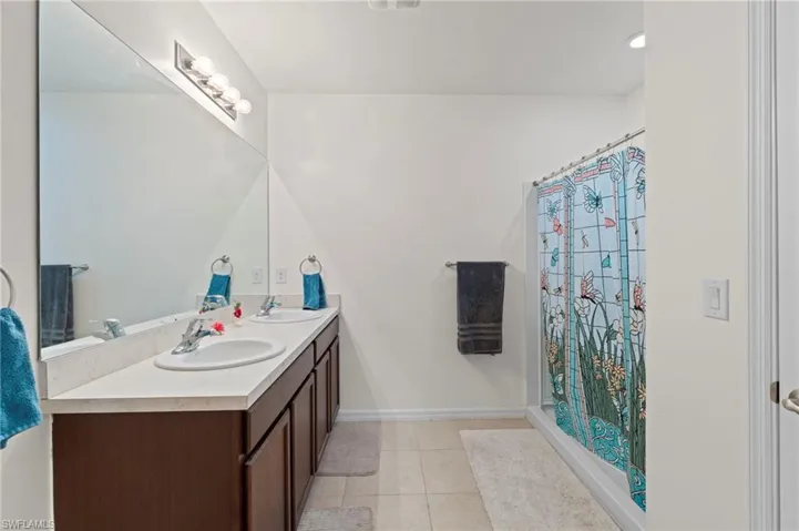 Bathroom with double vanity, light tile patterned floors, a shower with shower curtain, and recessed lighting
