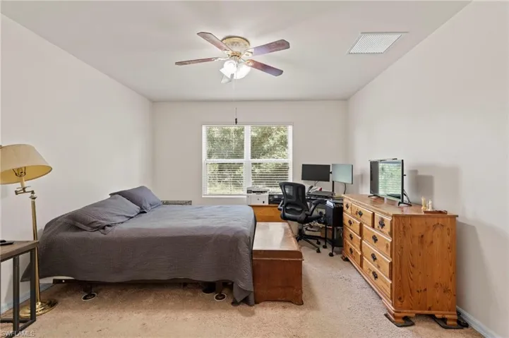 Bedroom with light carpet, ceiling fan, and an office area