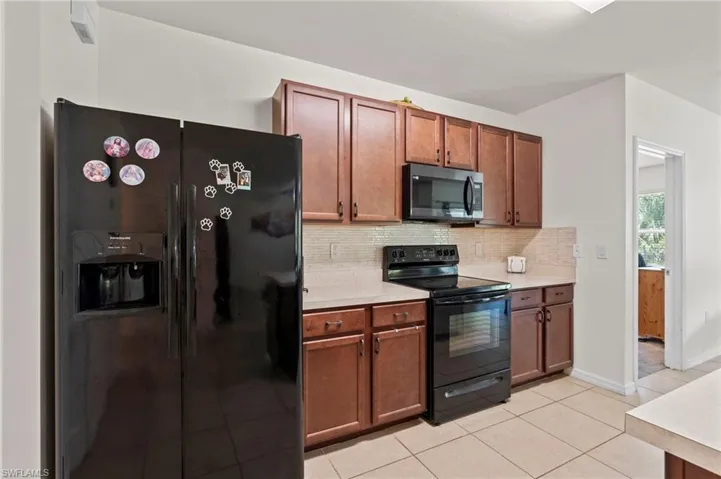 Kitchen with black appliances, light countertops, decorative backsplash, light tile patterned floors, and brown cabinets