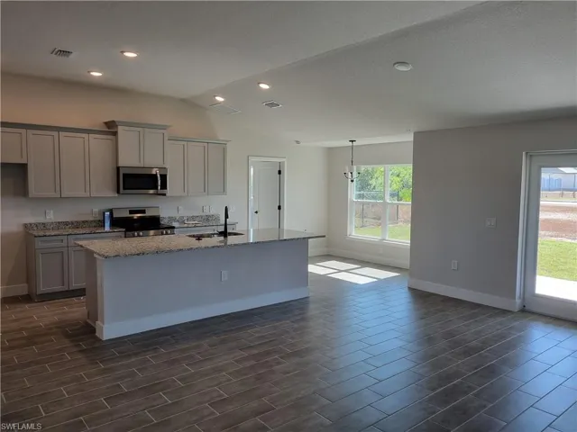 Kitchen with light stone countertops, a kitchen island with sink, appliances with stainless steel finishes, gray cabinetry, and wood finish floors