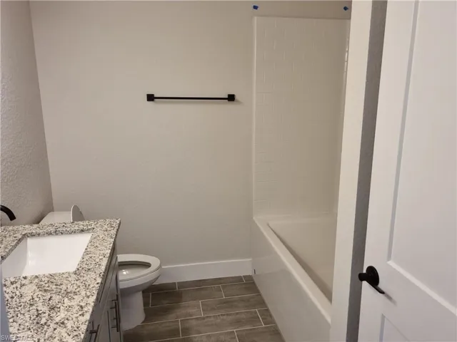 Full bath featuring vanity, a textured wall, wood tiled floors, and  shower combination
