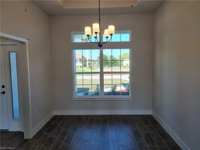 Unfurnished dining area with wood finish floors, a chandelier, and a tray ceiling