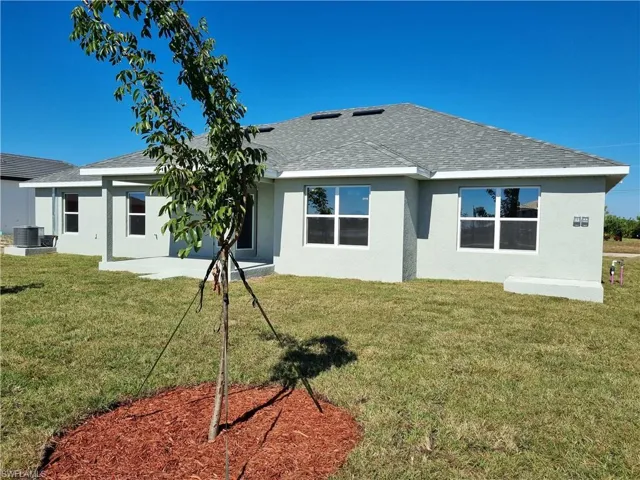Rear view of house with a shingled roof, stucco siding, a patio, and a lawn