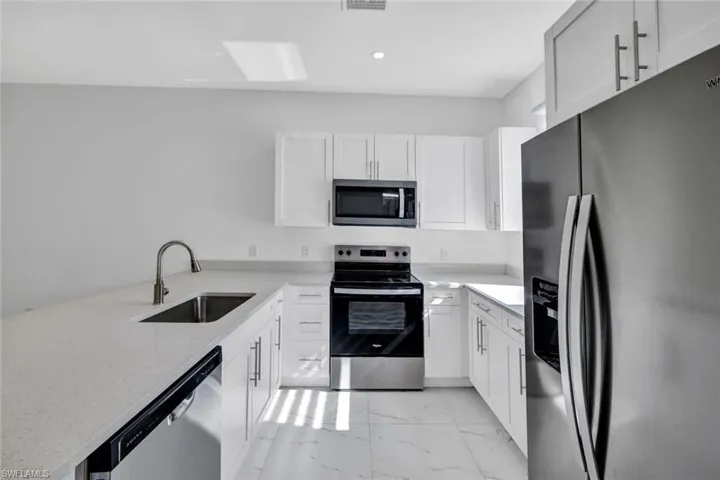 Kitchen featuring stainless steel appliances, light marble finish flooring, light stone counters, and white cabinetry