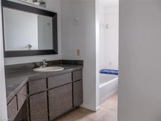 Full bath with vanity, light tile patterned floors, and washtub / shower combination