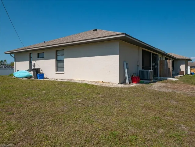 View of side of property with a yard, stucco siding, and roof with shingles