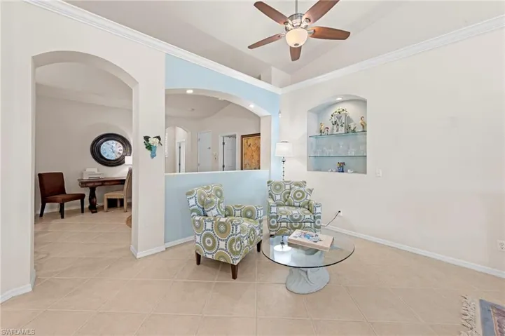 Sitting room with crown molding, light tile patterned flooring, a ceiling fan, arched walkways, and lofted ceiling