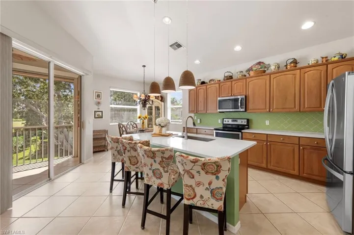 Kitchen with brown cabinets, backsplash, appliances with stainless steel finishes, light tile patterned floors, and hanging light fixtures