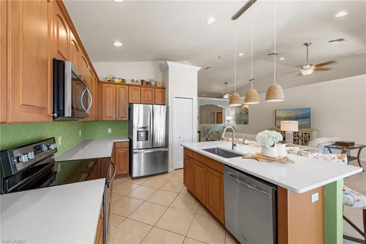Kitchen featuring stainless steel appliances, vaulted ceiling, light tile patterned flooring, hanging light fixtures, and tasteful backsplash
