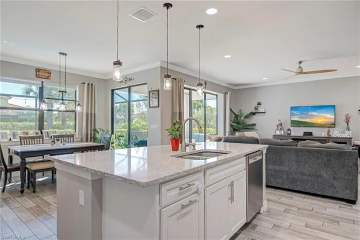 Kitchen with white cabinets, light stone countertops, decorative light fixtures, crown molding, and plank tile flooring