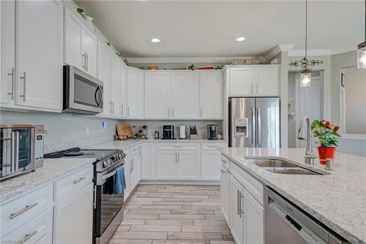 Kitchen with stainless steel appliances, white cabinetry, hanging light fixtures, and crown molding