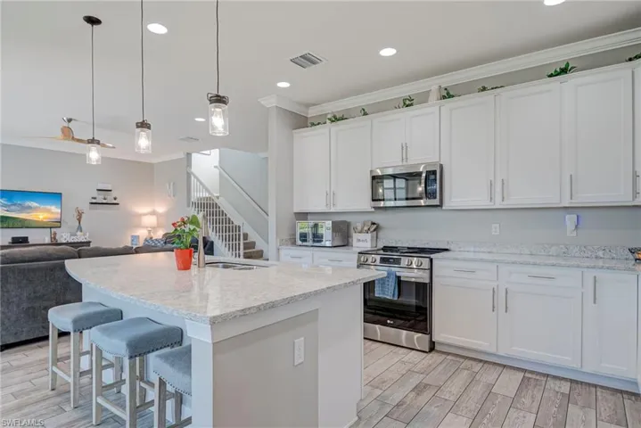 Kitchen with open floor plan, stainless steel appliances, a breakfast bar area, plank tile floors, and hanging light fixtures