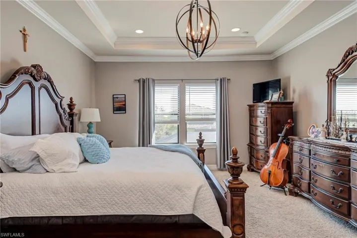 Carpeted bedroom with hanging lights, a raised ceiling, and ornamental molding