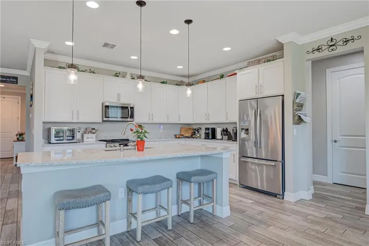 Kitchen featuring stainless steel appliances, hanging light fixtures, plank tiled floors, white cabinets, and ornamental molding