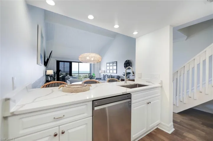 Kitchen featuring stainless steel dishwasher, light stone counters, white cabinets, vaulted ceiling, and dark wood-style flooring