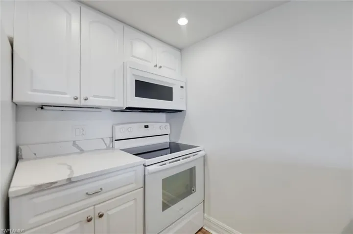 Kitchen with white appliances, white cabinets, recessed lighting, and light stone counters