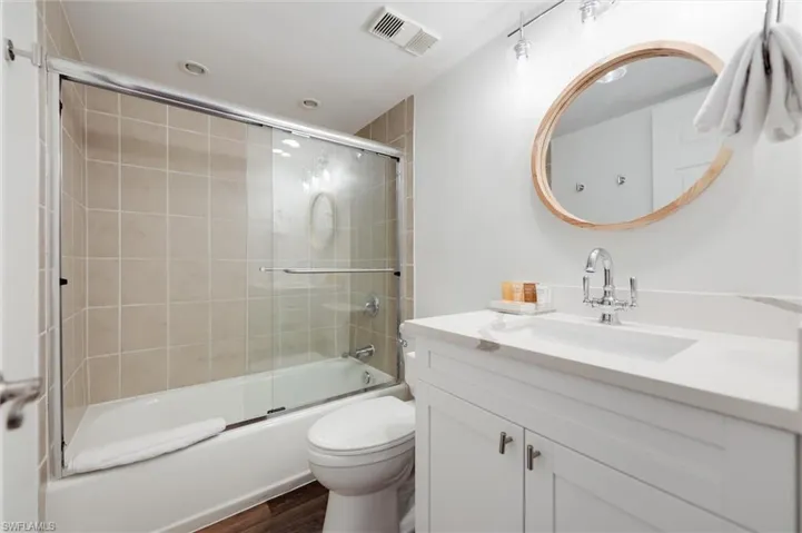 Full bathroom with vanity, shower / bath combination with glass door, and dark wood-style floors