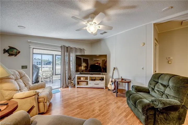 Living area with wood finished floors, crown molding, ceiling fan, and a textured ceiling