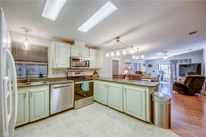 Kitchen featuring hanging light fixtures, a textured ceiling, a peninsula, open floor plan, and appliances with stainless steel finishes