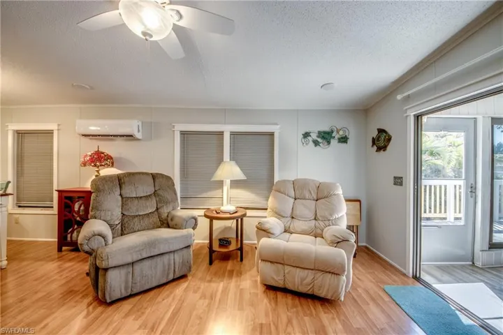 Living area featuring wood finished floors, a textured ceiling, a ceiling fan, and a wall unit AC