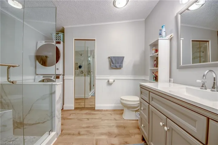 Full bathroom featuring crown molding, a textured ceiling, light wood finished floors, vanity, and a marble finish shower