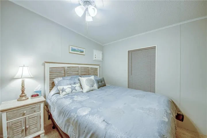 Bedroom with crown molding, a ceiling fan, lofted ceiling, carpet flooring, and a textured ceiling