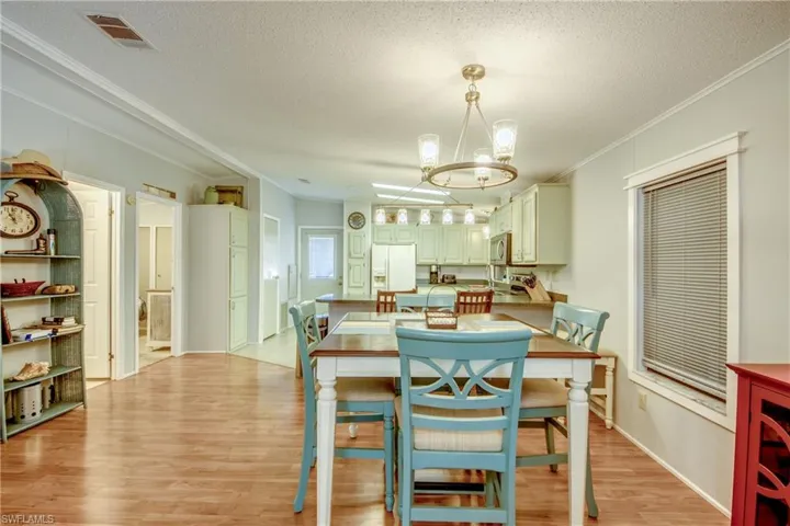 Dining space featuring ornamental molding, light wood-style flooring, a textured ceiling, and a chandelier