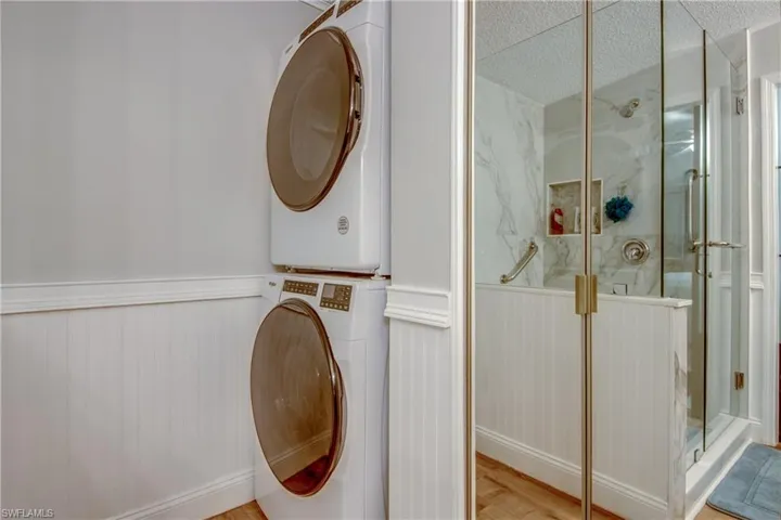 Laundry area featuring estacked washer and dryer, light wood finished floors, wainscoting, and a textured ceiling