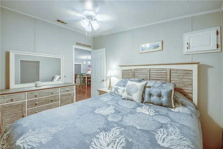 Bedroom featuring ornamental molding, a textured ceiling, ceiling fan, a decorative wall, and wood finished floors