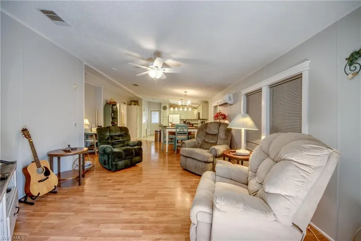 Living room featuring light wood-style floors, a ceiling fan, a textured ceiling, a wall unit AC, and a chandelier