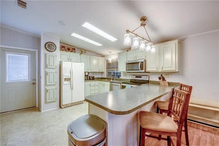 Kitchen featuring appliances with stainless steel finishes, hanging light fixtures, a kitchen bar, a textured ceiling, and a peninsula