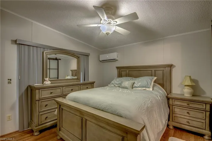 Bedroom with crown molding, light wood-style flooring, a textured ceiling, ceiling fan, and an AC wall unit