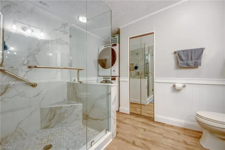 Bathroom featuring a marble finish shower, wood finished floors, a textured ceiling, wainscoting, and crown molding