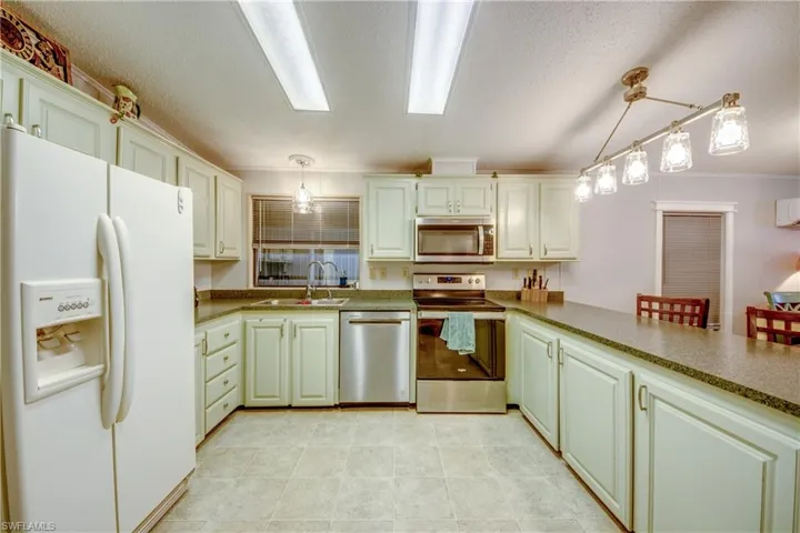 Kitchen featuring appliances with stainless steel finishes, a textured ceiling, a peninsula, pendant lighting, and dark countertops