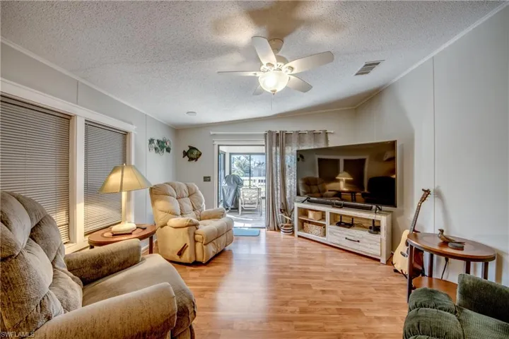Living room with light wood-style floors, crown molding, a ceiling fan, and a textured ceiling