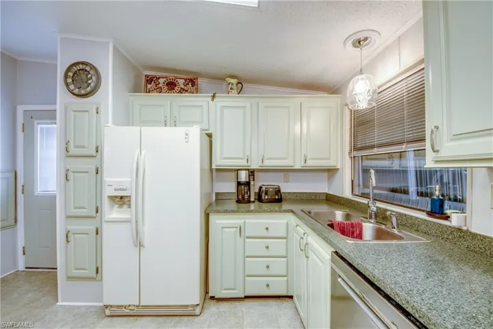 Kitchen with white fridge with ice dispenser, stainless steel dishwasher, hanging light fixtures, ornamental molding, and a textured ceiling