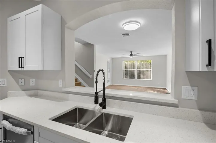 Kitchen with light stone counters, white cabinets, stainless steel dishwasher, and ceiling fan