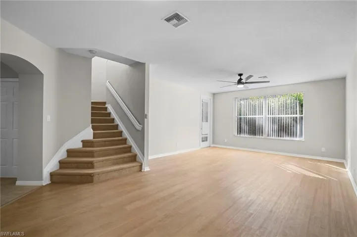 Unfurnished living room featuring light wood finished floors, stairs, ceiling fan, and arched walkways