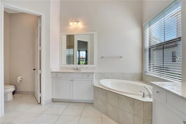 Bathroom featuring vanity, tiled bath, tile patterned flooring, and water closet