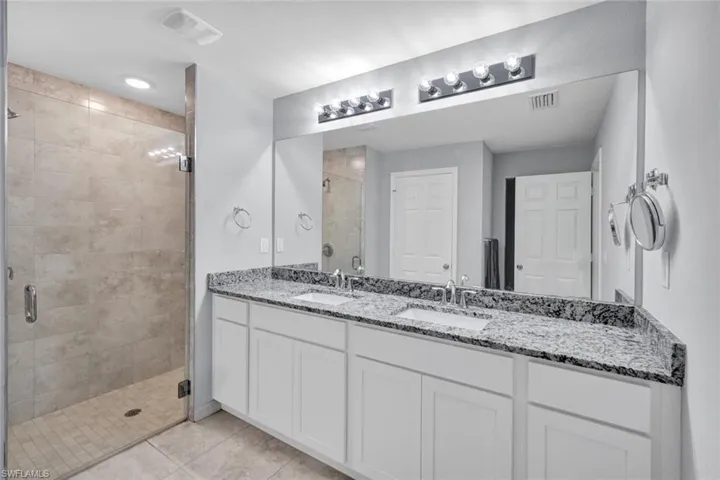 Bathroom featuring a stall shower, double vanity, and light tile patterned flooring