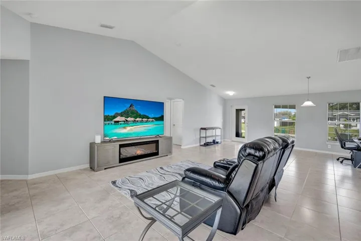 Living area featuring a glass covered fireplace, light tile patterned flooring, an office area, and high vaulted ceiling