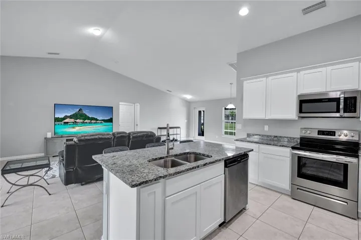 Kitchen featuring stainless steel appliances, white cabinetry, dark stone counters, open floor plan, and vaulted ceiling